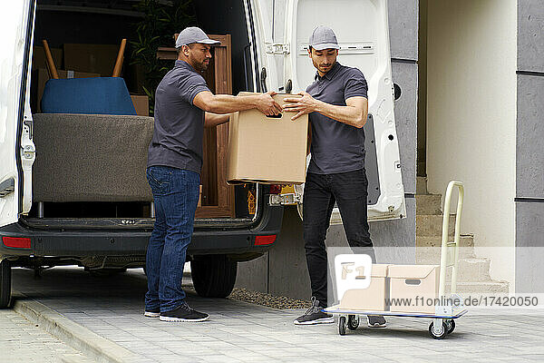 Man helping colleague while unloading boxes from van