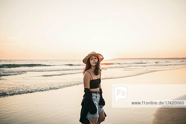 Junge Frau steht bei Sonnenuntergang am Strand