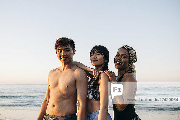 Smiling man with female friends standing at beach during sunset
