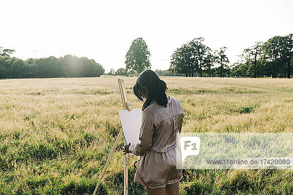 Woman painting on canvas while standing at park
