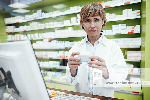Mature female pharmacist with bangs holding medicine at pharmacy store