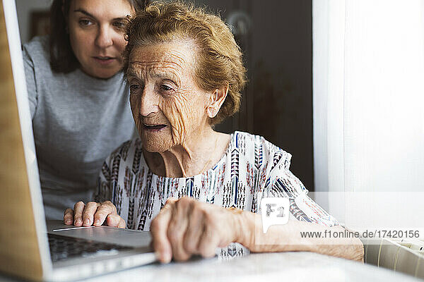 Enkelin hilft Großmutter  während sie zu Hause Laptop benutzt
