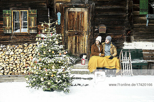 Paar schaut auf den Weihnachtsbaum  während es vor dem Bauernhaus sitzt