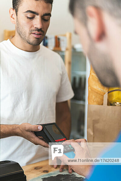 Male customer entering PIN while paying through credit card at shop