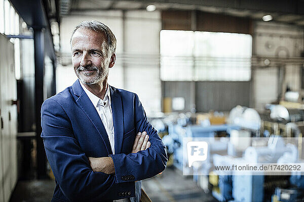 Smiling businessman standing with arms crossed at steel mill