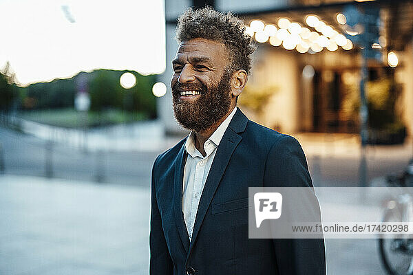Happy businessman with brown hair and beard standing on street