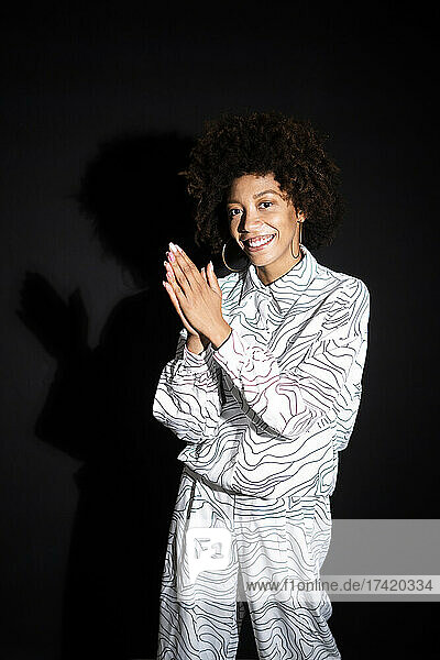 Smiling woman with hands clasped against black background