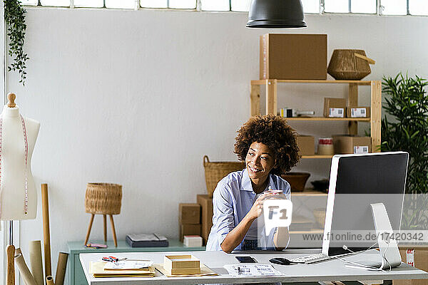 Smiling female design professional holding mug while sitting at desk in studio