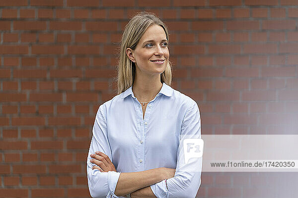 Thoughtful businesswoman with arms crossed in front of wall