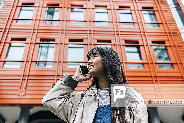 Young woman talking on mobile phone in front of building
