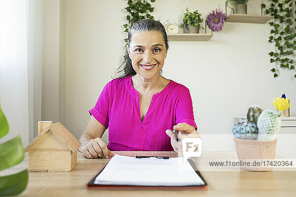 Smiling female real estate agent offering pen at home office