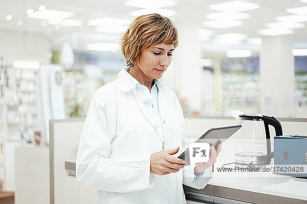 Female pharmacist using digital tablet while standing at medical store