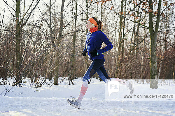 Woman running near bare trees during snow in winter