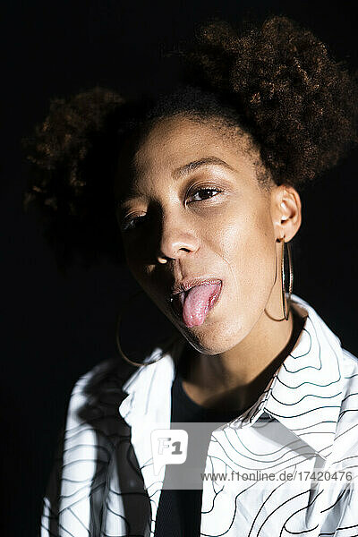 Playful woman sticking out tongue against black background