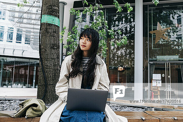 Young woman with laptop sitting in front of building