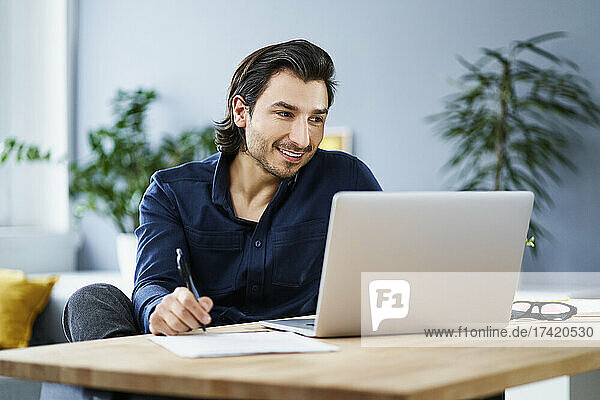 Businessman holding pen while working on laptop at home office