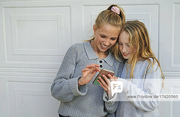 Smiling girls sharing mobile phone in front of garage door