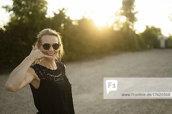 Lächelnde Frau macht bei Sonnenuntergang eine „Ruf mich“-Geste