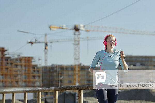 Junge Frau mit Kopfhörern joggt auf der Baustelle