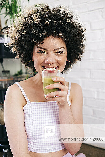 Smiling young woman holding smoothie glass while sitting at home