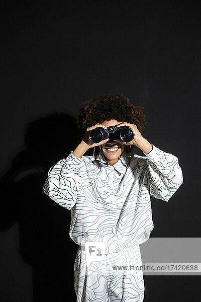 Smiling woman looking through binocular against black background