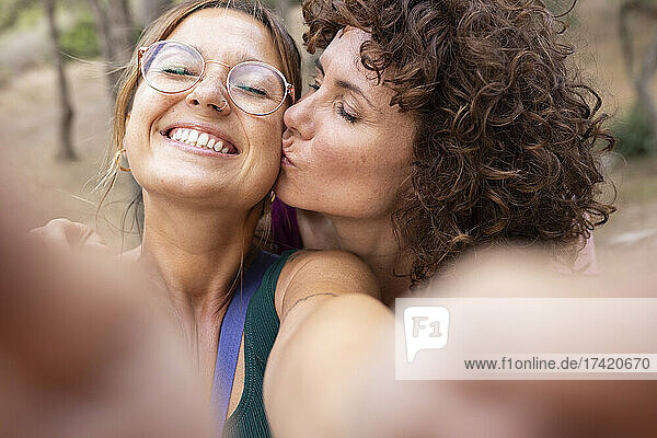 Smiling woman taking selfie with friend kissing on cheek
