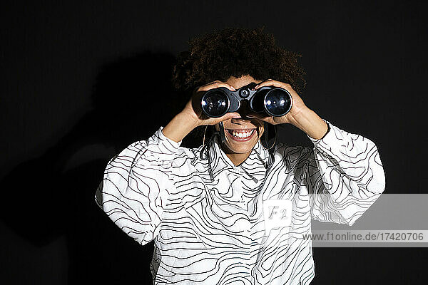 Woman looking through binocular against black background