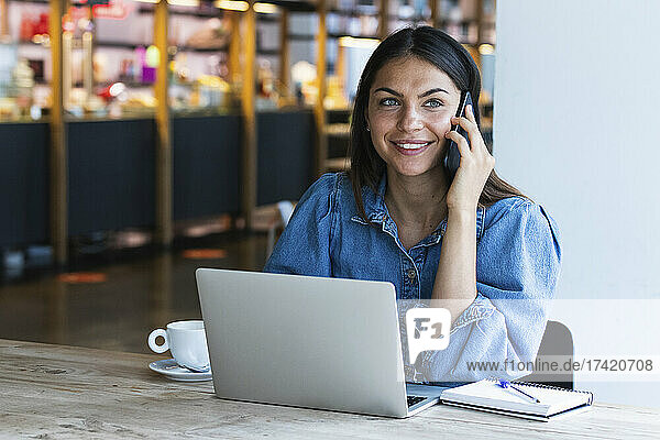Smiling young businesswoman talking on mobile phone at cafe