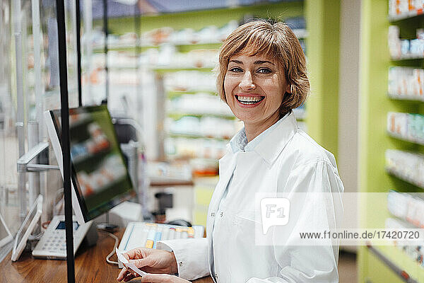 Happy female pharmacist standing in medical store