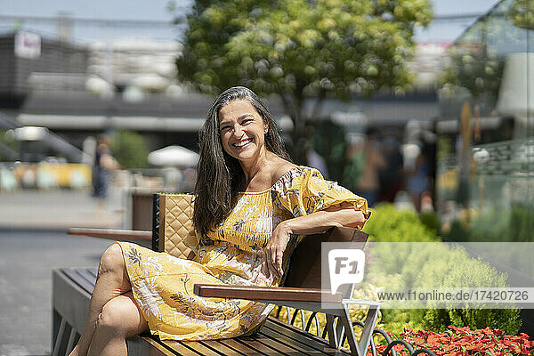 Happy mature woman sitting on bench during sunny day