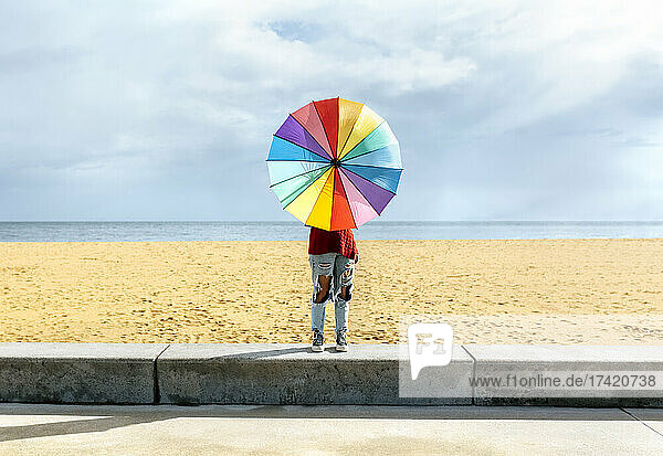 Woman holding umbrella while standing on wall in front of beach