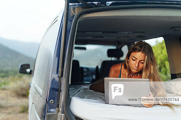 Woman with blond hair using laptop while relaxing in camper van