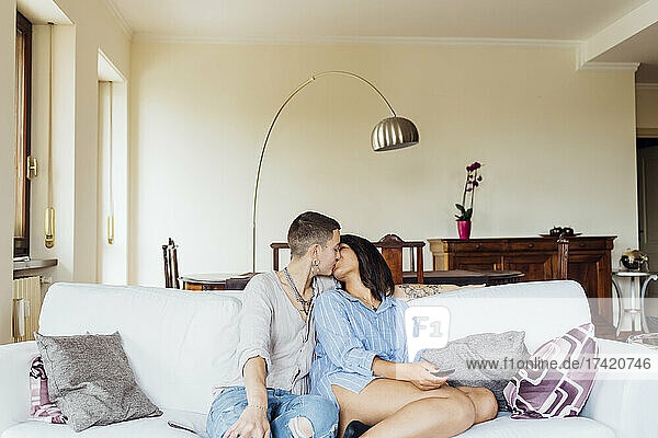 Affectionate girlfriends kissing while sitting on sofa in living room