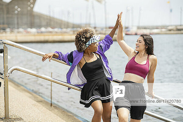 Multi-ethnic female friends giving high-five in front of railing