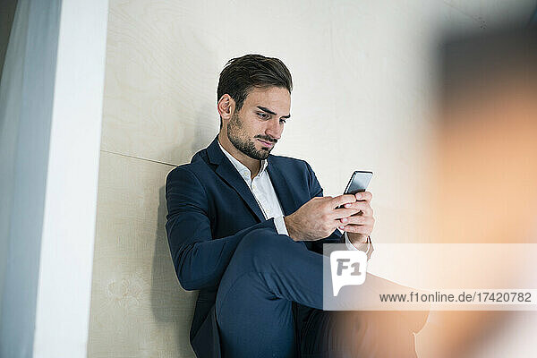 Young businessman text messaging through smart phone while sitting in office