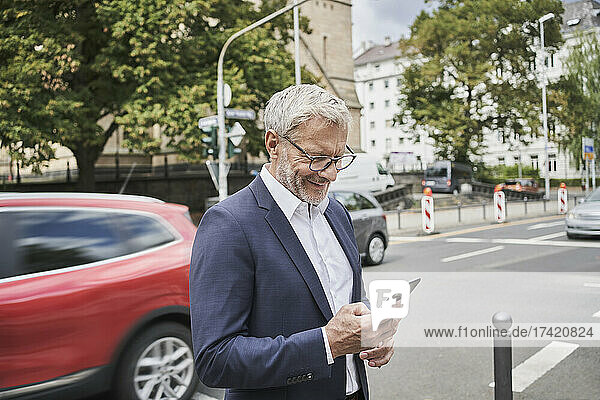 Smiling male professional using smart phone on road