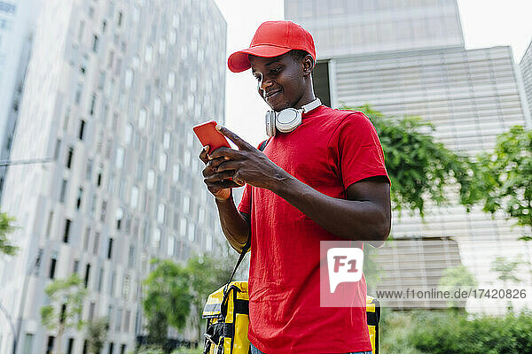 Smiling delivery man text messaging through smart phone in city