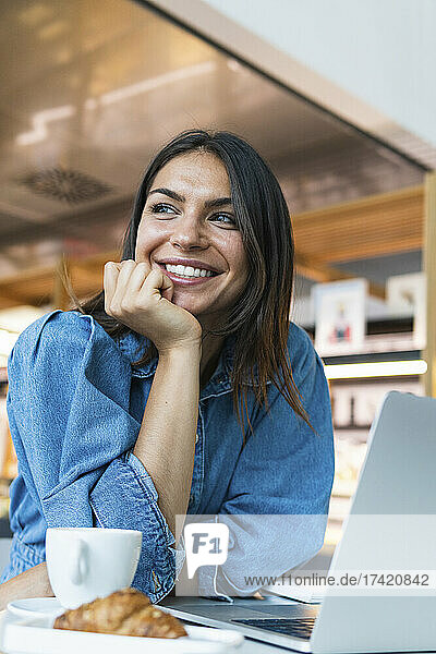 Beautiful businesswoman with hand on chin leaning on table at coffee shop