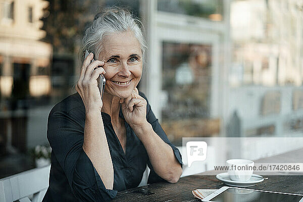 Smiling mature businesswoman talking on mobile phone in cafe
