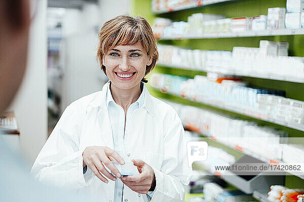 Lächelnde Apothekerin erklärt männlichen Kunden in der Apotheke Medikamente