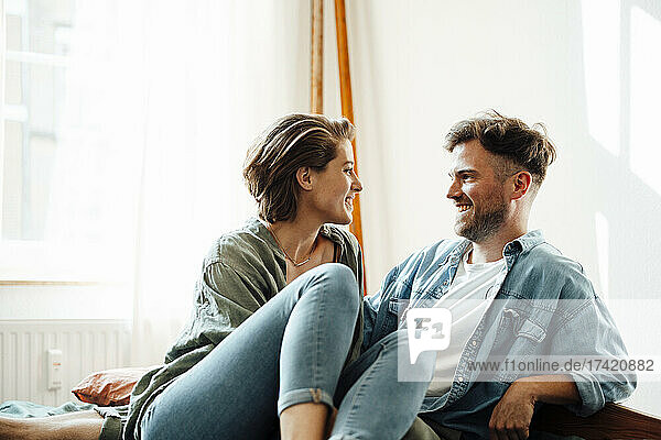 Smiling woman looking at man while sitting on bed at home
