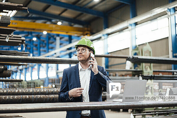 Businessman with hardhat talking on smart phone at metal industry