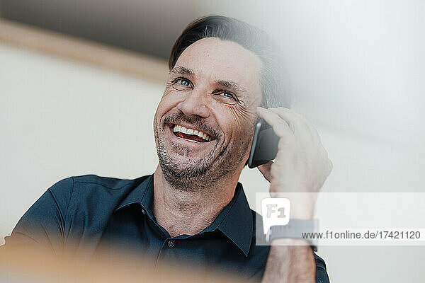 Mature businessman laughing while talking on smart phone at work place