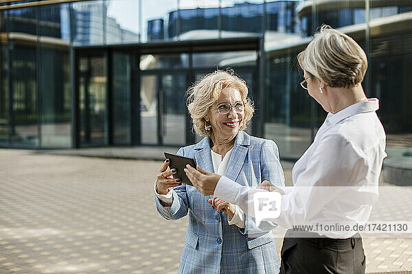 Female coworkers discussing over digital tablet while standing outside office building