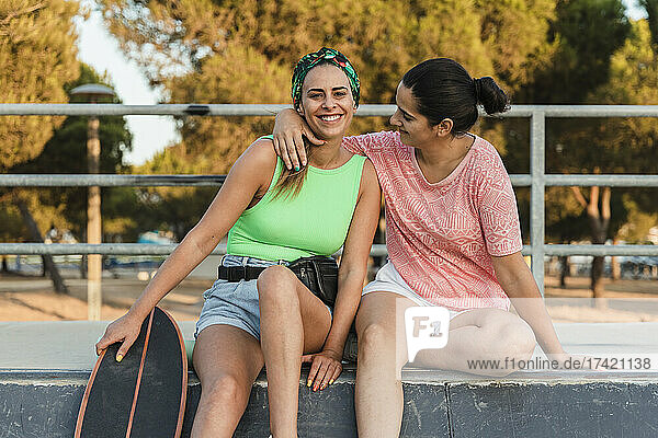 Woman sitting with arm around female friend at skateboard park