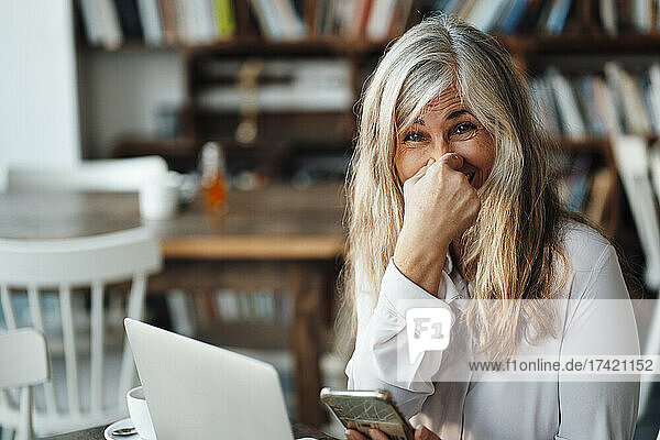 Geschäftsfrau hält Nase  während sie mit Smartphone und Laptop im Café sitzt