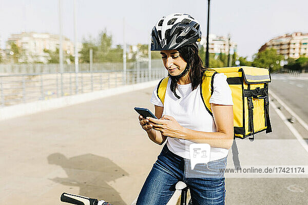 Female delivery person with bicycle using mobile phone on sunny day