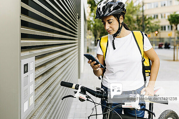 Female delivery person using mobile phone while standing by gate