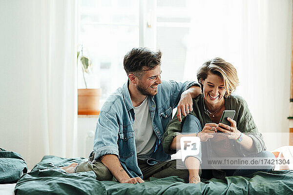 Man sitting with woman using smart phone on bed at home