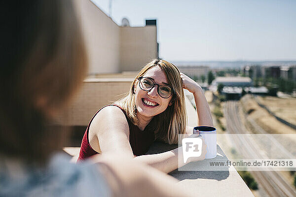 Smiling businesswoman looking at colleague while leaning on retaining wall during sunny day